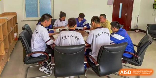 A small group of students from Dalian No.24 High School Cambridge International A-Level Centre and a teacher are seated around a table for a focused discussion or meeting.