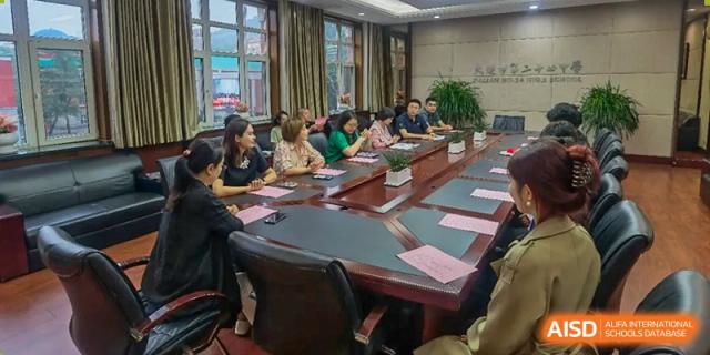 A group of faculty or staff members from Dalian No.24 High School Cambridge International A-Level Centre are seated around a large, dark wood table during a meeting.