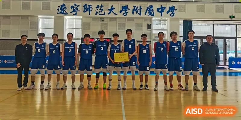 A boys' indoor volleyball or basketball team from Dalian No.24 High School Cambridge International A-Level Centre poses together in a gymnasium, all wearing matching blue and white uniforms and holding a trophy or award.