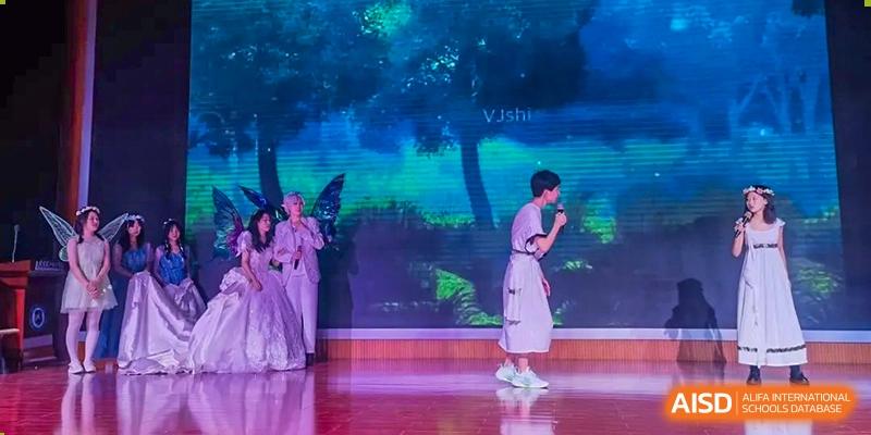 A student from Dalian No.24 High School Cambridge International A-Level Centre bows on a stage during a performance with a dark, artistic blue and green light backdrop.