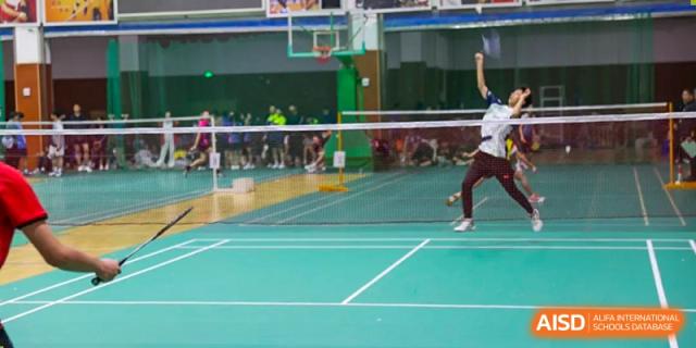 A student from Dalian No.24 High School Cambridge International A-Level Centre leaps to hit a shuttlecock while playing badminton on an indoor green court.