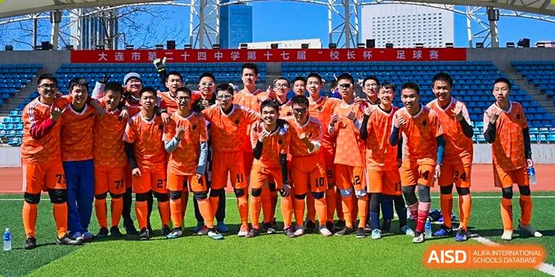 A boys' soccer team from Dalian No.24 High School Cambridge International A-Level Centre, wearing bright orange jerseys, poses for a team photo outdoors.