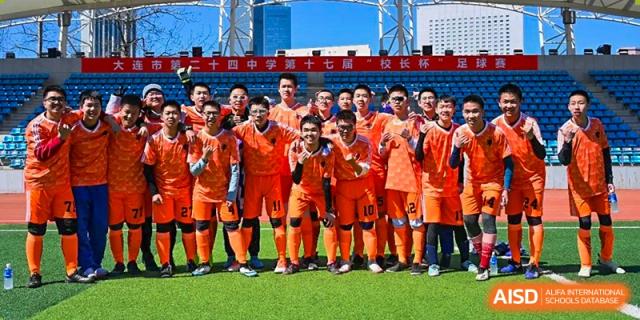 A boys' soccer team from Dalian No.24 High School Cambridge International A-Level Centre, wearing bright orange jerseys, poses for a team photo outdoors.