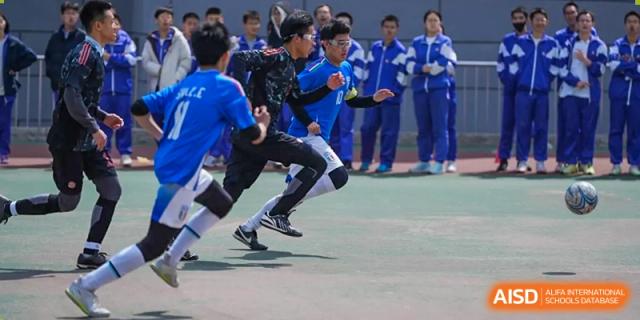 A student from Dalian No.24 High School Cambridge International A-Level Centre, wearing a black and blue outfit, leaps while participating in an outdoor sports activity.