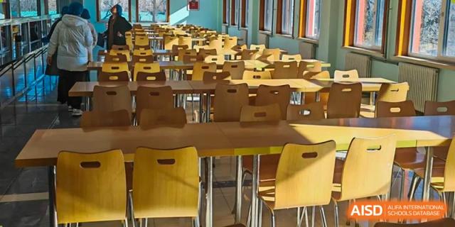 An empty cafeteria or dining hall at Dalian No.24 High School Cambridge International A-Level Centre with rows of light wood tables and chairs.