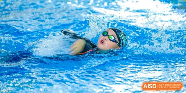 A student wearing goggles and a swim cap swimming freestyle in the pool at Dehong International Chinese School.