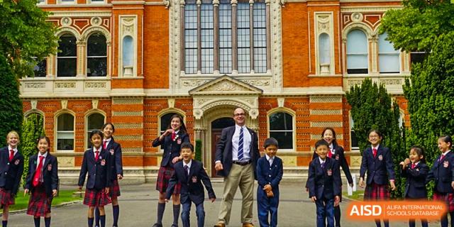 A group of students and a teacher from Dulwich College Shanghai Puxi standing outside the school building.
