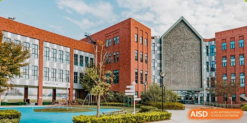 The exterior of a building at Dulwich College Shanghai Puxi with trees and a sidewalk.