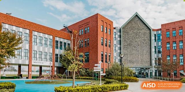 The exterior of a building at Dulwich College Shanghai Puxi with trees and a sidewalk.