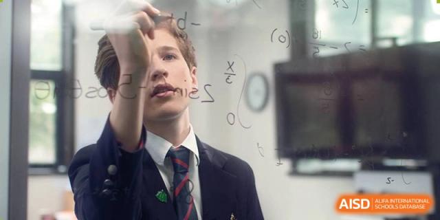 A male student at Dulwich College Suzhou is seen looking up and writing a mathematical equation on a whiteboard during a class.