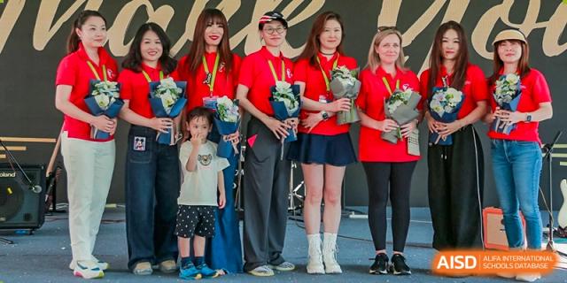 Students from Dulwich College Suzhou are standing together in red shirts holding bouquets of flowers and looking happy.