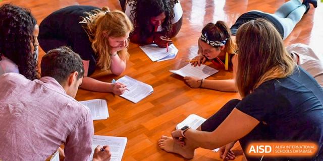 A group of students from Dulwich College Suzhou are sitting on the floor in a classroom, gathered around papers and collaborating on an assignment.
