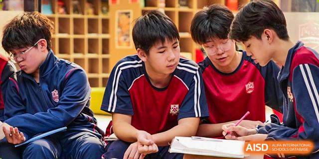 Two male students at Dulwich College Suzhou are in a classroom, with one student in a red sports jersey looking down at a book.