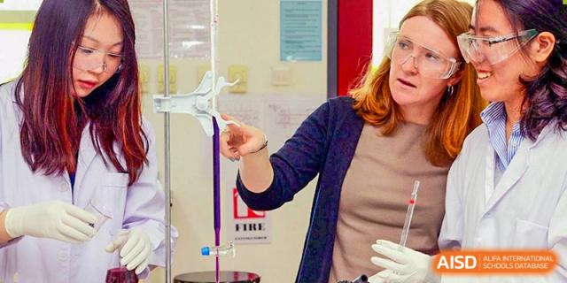 A teacher or student at Dulwich College Suzhou is demonstrating a science experiment, pouring a purple liquid from a burette into a beaker.