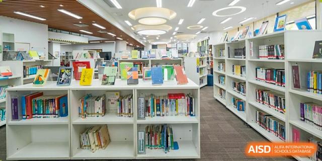 A brightly lit library at Dulwich College Suzhou with white bookshelves filled with books.