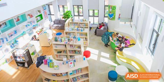 A brightly lit children's library at Dulwich College Suzhou with low, curved bookshelves and an inviting reading area with a couch.