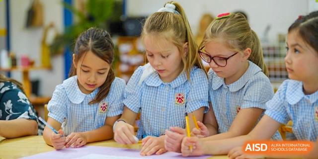 A group of young female students at Dulwich College Suzhou are sitting at a desk and drawing on paper with pencils.