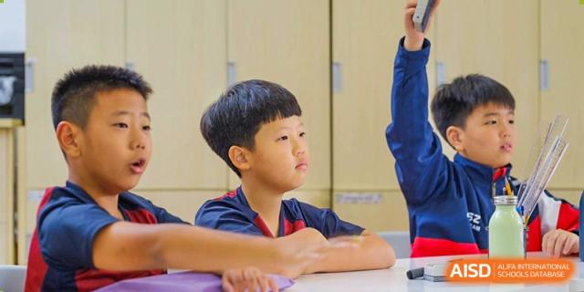 A young male student at Dulwich College Suzhou sits at a desk, looking thoughtfully off to the side.