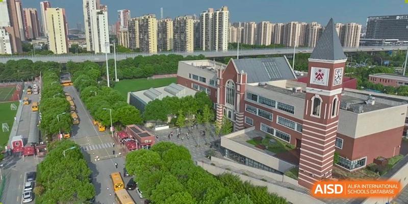 An aerial view of a large school building with students outside, surrounded by apartment buildings at Dulwich College Suzhou.