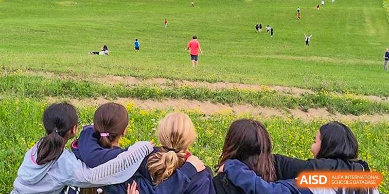 Two students sit on a grassy hill looking out at a field where other students are playing at Dulwich College Suzhou.