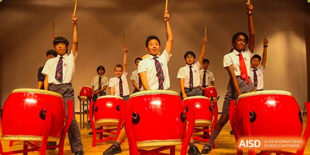 Students from Dulwich College Suzhou perform a traditional drum routine on large red drums.