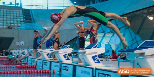 A Dulwich College Suzhou swimmer dives from a starting block into a pool during a competition.