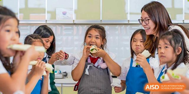 A young female student at Dulwich College Suzhou is happily eating something she has made in a cooking class.