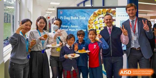 A group of students and a teacher at Dulwich College Suzhou are standing together, holding plates of pies at a "Pi Day Bake Sale."