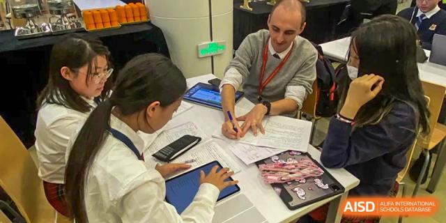 A teacher from Dulwich International Suzhou High School Programme helping two students with their work, which includes a tablet.