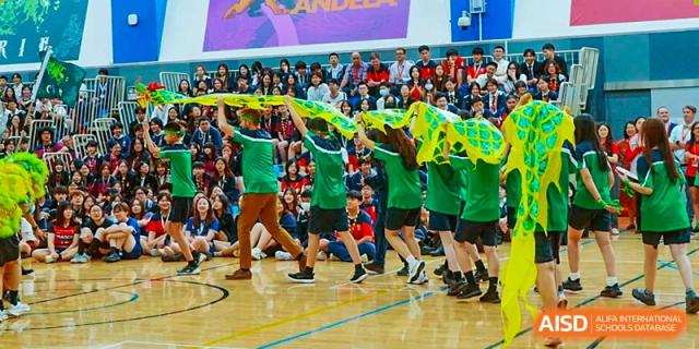 A group of students from Dulwich International Suzhou High School Programme cheering and dancing with green and yellow flags during a school event.