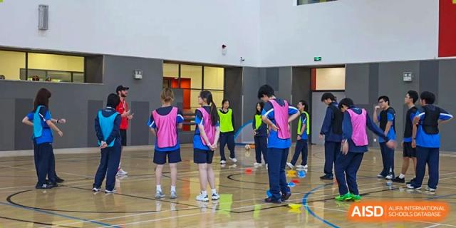 A group of students from Dulwich International Suzhou High School Programme participating in a sports activity indoors.