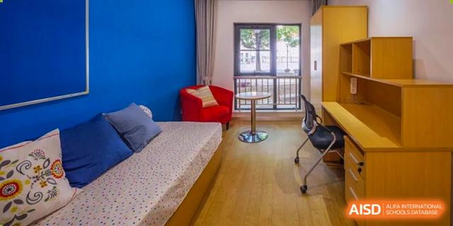 A student's bedroom at Dulwich International Suzhou High School Programme, featuring a bed, a desk, and a red armchair.