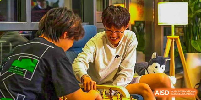 A high school student from Dulwich International Suzhou High School Programme smiles while playing a game of chess with a friend.