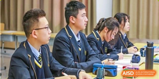 A group of Grand International School students in uniform attentively listening to a lesson in a classroom.