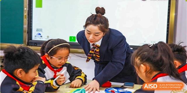 A Grand International School teacher assisting two younger students with a colorful educational toy or project.
