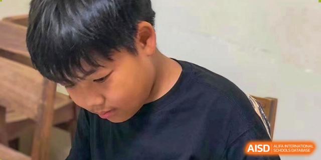 A close-up profile of a male Grand International School student looking down intently at his work or a book.