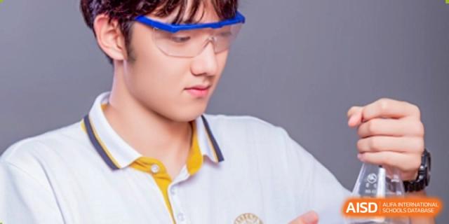 A male Grand International School student wearing safety goggles in a science lab, focusing on an experiment or item.