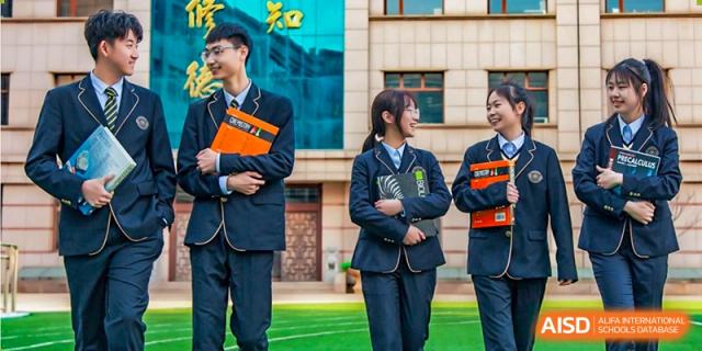 Several Grand International School students in dark blue uniforms and ties smiling and walking together outdoors on campus, holding books and notebooks.