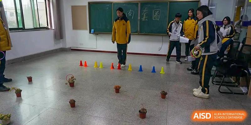 Grand International School students in uniform standing in a line of cones in a classroom or gym during a physical education or obstacle course activity.