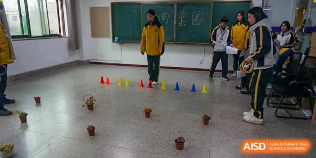 Grand International School students in uniform standing in a line of cones in a classroom or gym during a physical education or obstacle course activity.