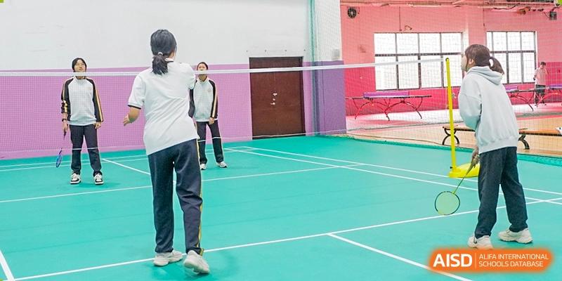 A Grand International School student playing badminton in an indoor court, holding a racket and facing a net.