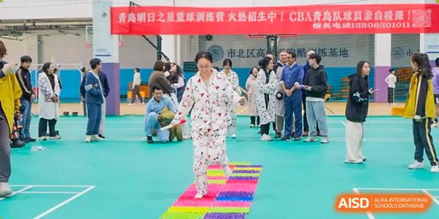 A woman in pajamas walking cautiously across a colorful textured mat during a fun or team-building activity at Grand International School.