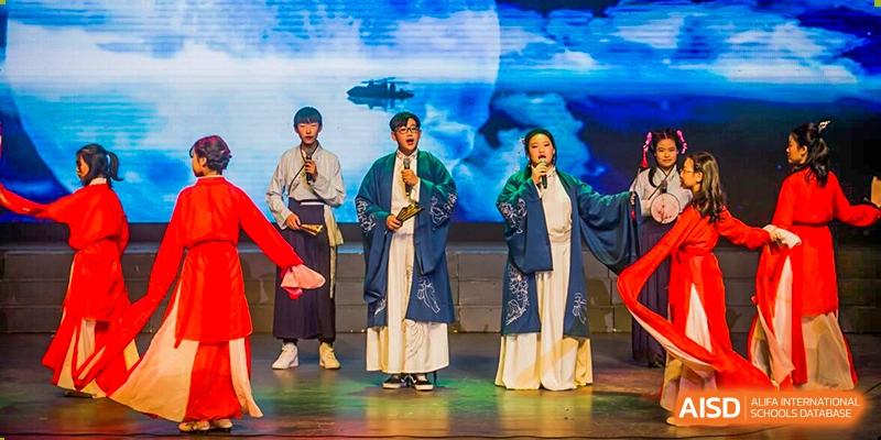 Grand International School students or performers in traditional Chinese attire singing or performing on a brightly lit stage.