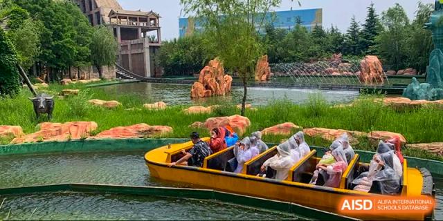 A group of Grand International School students and adults riding a boat ride through a themed outdoor area, likely on a school trip.