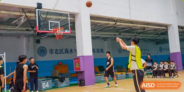 Grand International School students practicing or playing basketball on an outdoor court near a wall with a mural.