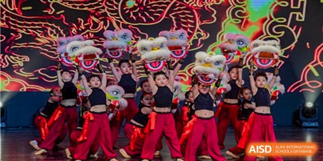 A performance featuring several Lion Dance costumes being operated by students wearing red pants and black tops at a Grand International School cultural event.