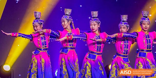 Grand International School students performing a traditional dance with buckets or containers balanced on their heads, wearing brightly colored costumes.