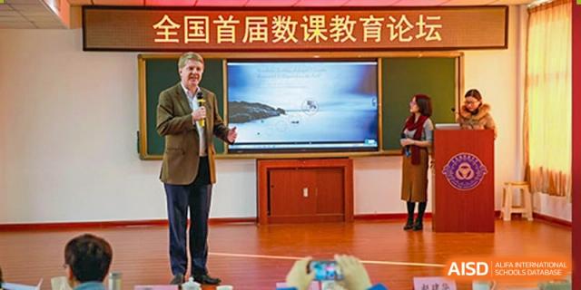 An international speaker or expert giving a presentation with a large screen in the background at an education forum hosted by Grand International School.