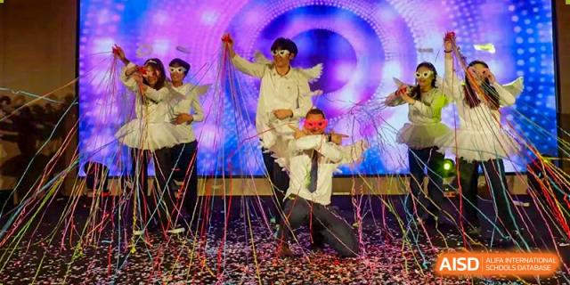 Two performers from Grand International School in light-colored costumes, with one performer hoisted on the other's shoulders amidst a shower of confetti.