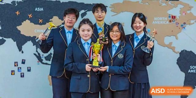 A group of Grand International School students in dark blue and gold uniforms posing with a trophy, celebrating an achievement.